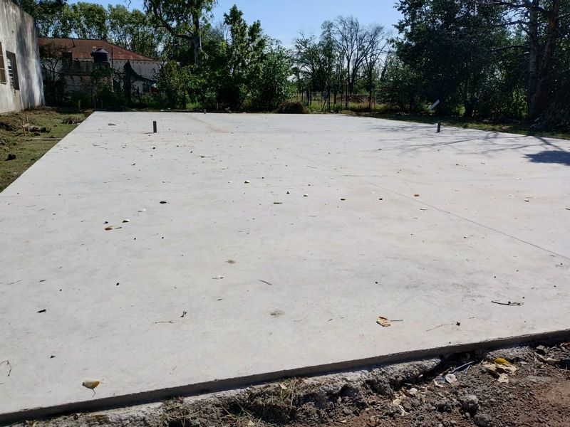 Platea de hormigón terminada sobre terreno, con arboleda al fondo
